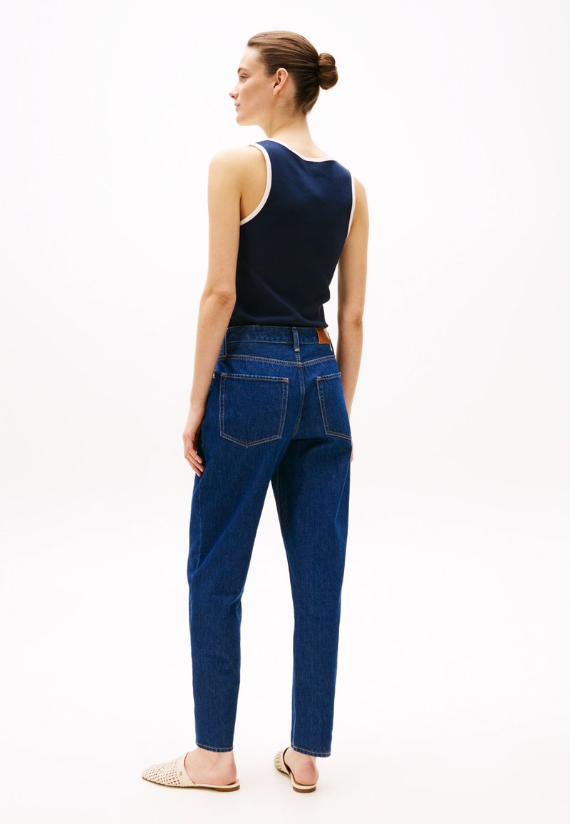 Granatowy top bez rękawów z białymi wykończeniami, niebieskie dżinsowe spodnie o wysokim stanie oraz beżowe buty wsuwane. Charakteryzuje się luźnym fasonem i dwiema tylnymi kieszeniami.