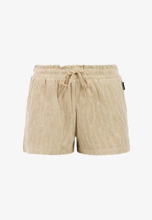 Lachend meisje dat met de hand op de heup staat, draagt een beige vissershoed, een turquoise top met korte mouwen, beige korte broek en beige sandalen op een witte achtergrond.