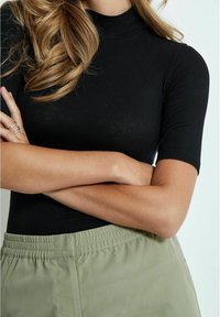 Top negro de manga corta con textura acanalada y cuello alto, combinado con pantalones verdes oliva con cintura elástica, que destacan una silueta ajustada.