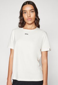 White cotton T-shirt featuring a crew neck, short sleeves, and a black "BOSS" print on the chest. Subtle colored accents on the sleeve.