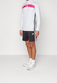 Långärmad, ljusgrå atletisk topp med en rosa rand och svarta detaljer, ihopparad med svarta shorts med rosa detaljer och tre ränder.