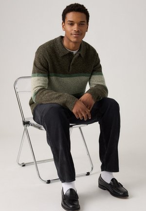 Knit pullover with a collar in dark green, light green, and cream stripes, paired with dark pants and black loafers, seated on a metallic chair.