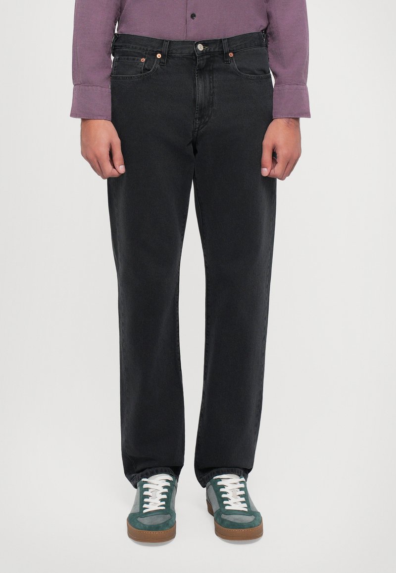 Zwarte denim jeans met een rechte snit, koperen klinknagels op de zakken, gecombineerd met groene en grijze sneakers met witte veters en een gestructureerde zool.