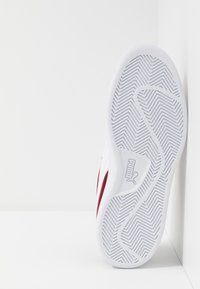 Bílá a červená podrážka tenisky Puma směřující dopředu s podrobným vzorem prořezu na bílém pozadí v rohu.