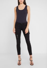 Svarta cargo byxor med blixtlåsdetaljer, figurnära design och fickor. Kombineras med en mörk tanktop och svarta remsandaler.