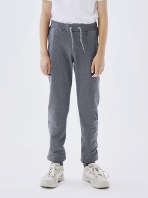 Pantalones gris de chándal con cinturilla elástica y cordón. Cuenta con bolsillos laterales, piernas ajustadas y puños de canalé en los tobillos. Combinados con zapatillas beige.