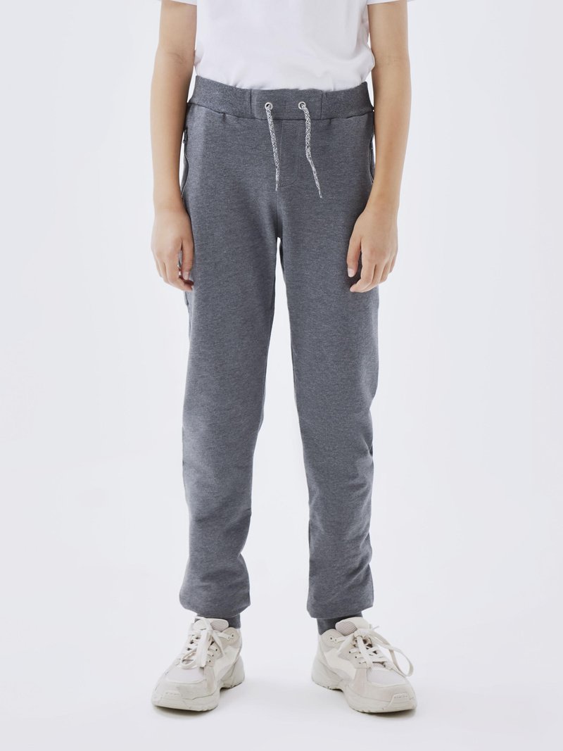 Grå joggebukser med elastisk midje og snøring. Har sidelommer, smalner inn mot leggen og ribbestrikkede ankler. Brukt med beige joggesko.