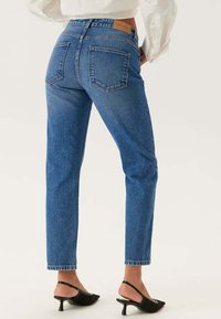 Blå denimjeans med hög midja och rak benmodell. Har två bakfickor och en brun läderetikett vid midjan.