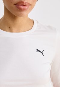 Bijela pamučna majica s okruglim izrezom i kratkim rukavima, s malim crnim Puma logotipom na prsima. Glatka tekstura.