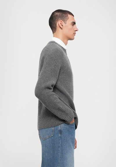 Pull en tricot côtelé gris avec un col rond, associé à un jean en denim bleu clair. Le tissu a une finition texturée. Coupe plate et décontractée.