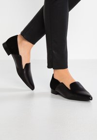 Svarta läder slip-on skor med spetsig tå och urgröpta detaljer. Har en låg klack och mockadetaljer bak för texturkontrast.