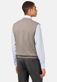 Svetlosivý pletený sveter s okrúhlym výstrihom, nosený cez svetlomodrú dlhú košeľu, doplnený tmavosivými nohavicami.