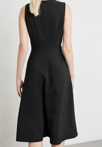 Schwarzes ärmelloses Kleid mit tailliertem Oberteil und ausgestelltem Midilänge-Rock, aus glattem strukturiertem Stoff mit dezenten Nahtdetails.