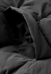 Tmavošedý, mäkký prikrývka so soft inner lining, prešívanou textúrou a hladkým vonkajším materiálom so zhrnutými okrajmi.
