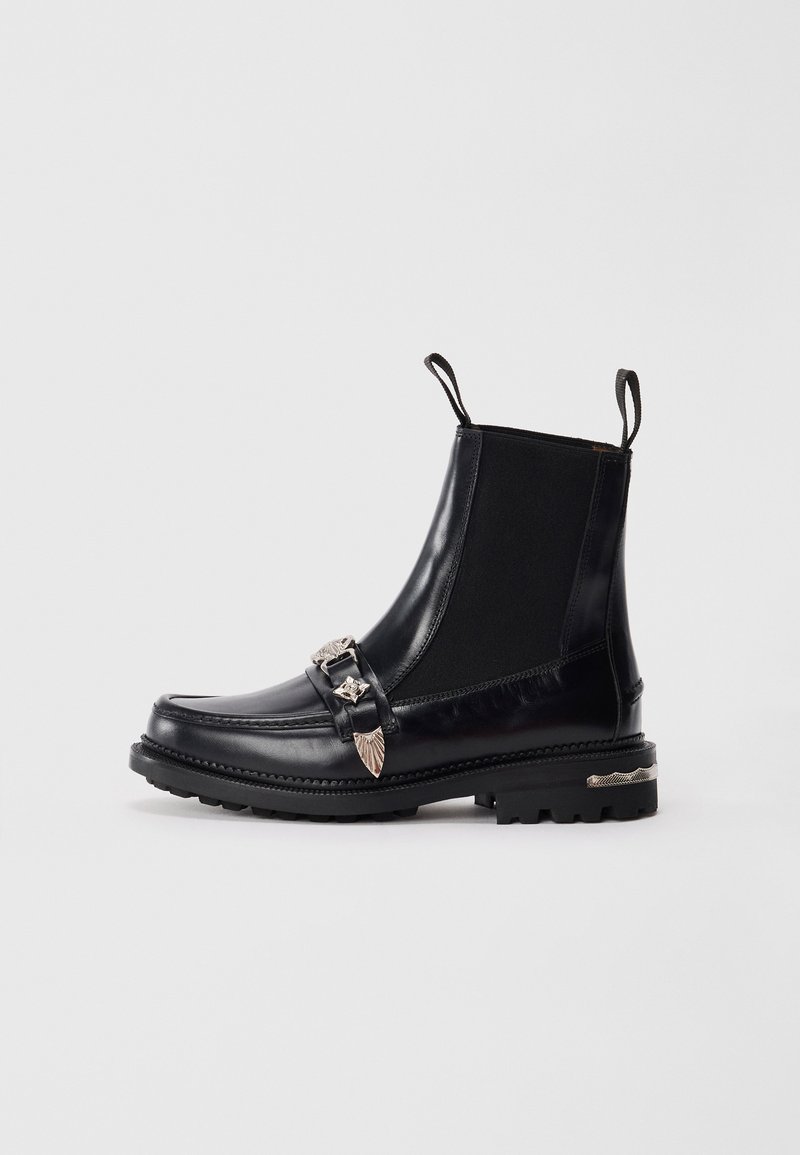 Bottines noires en cuir avec des panneaux élastiques sur les côtés, une boucle décorative en argent avec des accents de feuilles et une semelle robuste pour une bonne adhérence.