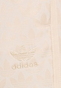 Béžová mikina Adidas s texturovaným květinovým vzorem, s vyšitým logem a tónovými akcenty na látce.