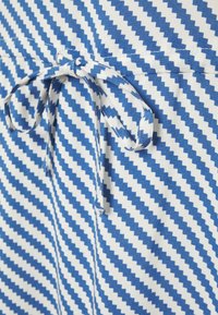 Modrá a bílá látka s vzorem a cik-cak pruhy, se zavázanou mašlí. Materiál vypadá texturovaně a tkaně.