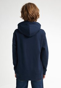 Mörkblå huvtröja med foder i huvan, långa ärmar och ribbade muddar. Vadderad bomullstextil med en mjuk yta. Inga framträdande logotyper eller mönster synliga.