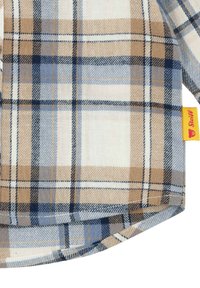 Tela de cuadro en tonos marrón, azul y blanco con una textura suave; presenta un dobladillo redondeado y una etiqueta roja con el nombre de la marca.