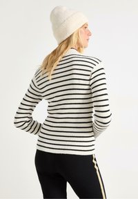 Sort og hvid stribet ribbet sweater med lange ærmer, båret med sorte bukser med gyldne sidelister, parret med en cremefarvet hue.