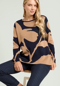 Maglione a maglia in blu navy e beige con un audace motivo floreale, scollatura rotonda e vestibilità rilassata. Abbinato a pantaloni navy a righe.