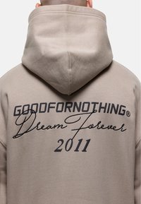 Felpa beige con una grande stampa nera sul retro, che presenta "GOODFORNOTHING," "Dream Forever," e "2011," in diversi caratteri e dimensioni.