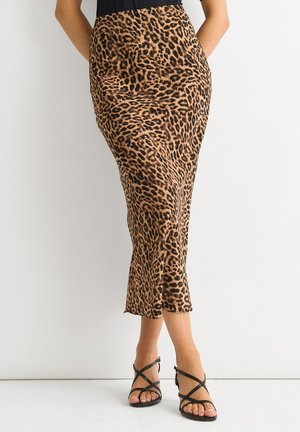 Gonna midi in stampa leopardata realizzata in tessuto leggero, silhouette aderente con spacco all'orlo, abbinata a sandali neri con cinturini.
