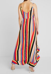 Monivärinen maksimekko, jossa on pystysuorat raidat punaisena, keltaisena, sinisenä ja mustana. Spagettiremmit ja matala selkädesign, vaate virtaa helmassa.