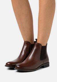 Bottes basses en cuir marron avec panneaux élastiques sur les côtés et une languette au talon. Elles présentent un bout arrondi et un talon bas et plat pour plus de confort.