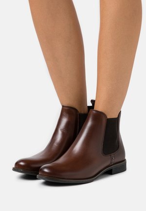 Bottes basses en cuir marron avec panneaux élastiques sur les côtés et une languette au talon. Elles présentent un bout arrondi et un talon bas et plat pour plus de confort.