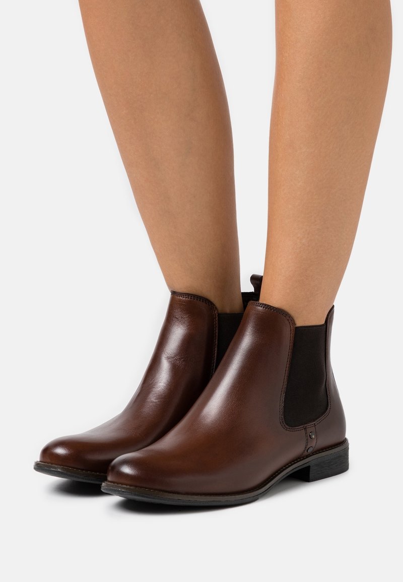 Bottes basses en cuir marron avec panneaux élastiques sur les côtés et une languette au talon. Elles présentent un bout arrondi et un talon bas et plat pour plus de confort.