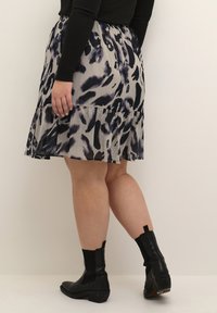Jupe évasée et à volants en gris avec des motifs abstraits noirs et violets. Associée à des bottines noires avec des côtés élastiques et des talons bas.