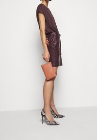 Jupe en cuir d'un violet profond, assortie à un haut sombre uni. Accessoire : petite pochette texturée en orange doux. Talons hauts en imprimé serpent complémentaires.