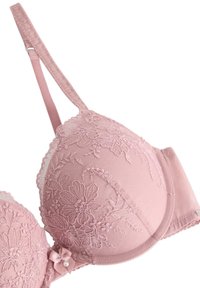 Vaaleanpunainen pitsirintaliivien, jossa on kukka-ompelua, muotoiltu malli, säädettävät olkaimet ja pieni kulkusolmuke etuosassa.