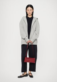Grijze zip-up hoodie, zwarte henley-shirt, marineblauwe wide-leg broek en zwarte instappers. Een rode rechthoekige handtas accentueert de outfit.