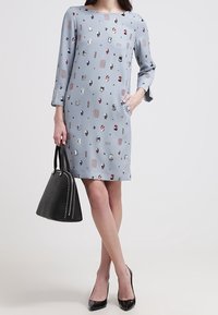 Jasnoniebieska sukienka z krótkim rękawem w różnorodne kolorowe wzory, zestawiona z czarną torebką z wypukłymi akcentami.