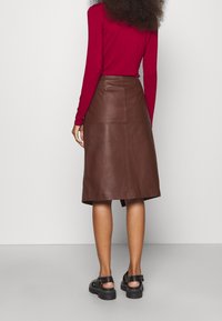 Ruskea nahkainen midi-hame, jossa suora leikkaus, takahalkio ja sileä pinta, yhdistetty mustiin paksupohjaisiin sandaaleihin.