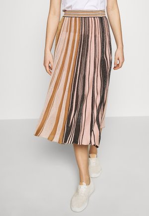 Femme portant une jupe midi plissée avec des rayures verticales marron, rose et noires, associée à des baskets blanches et un haut blanc.