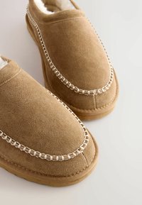 Pruunist nahast sisetossud pehme sisevoodriga, millel on valged õmblused, mis rõhutavad kaardus äärt, ja lapikud tallad mugavaks jalavahele.