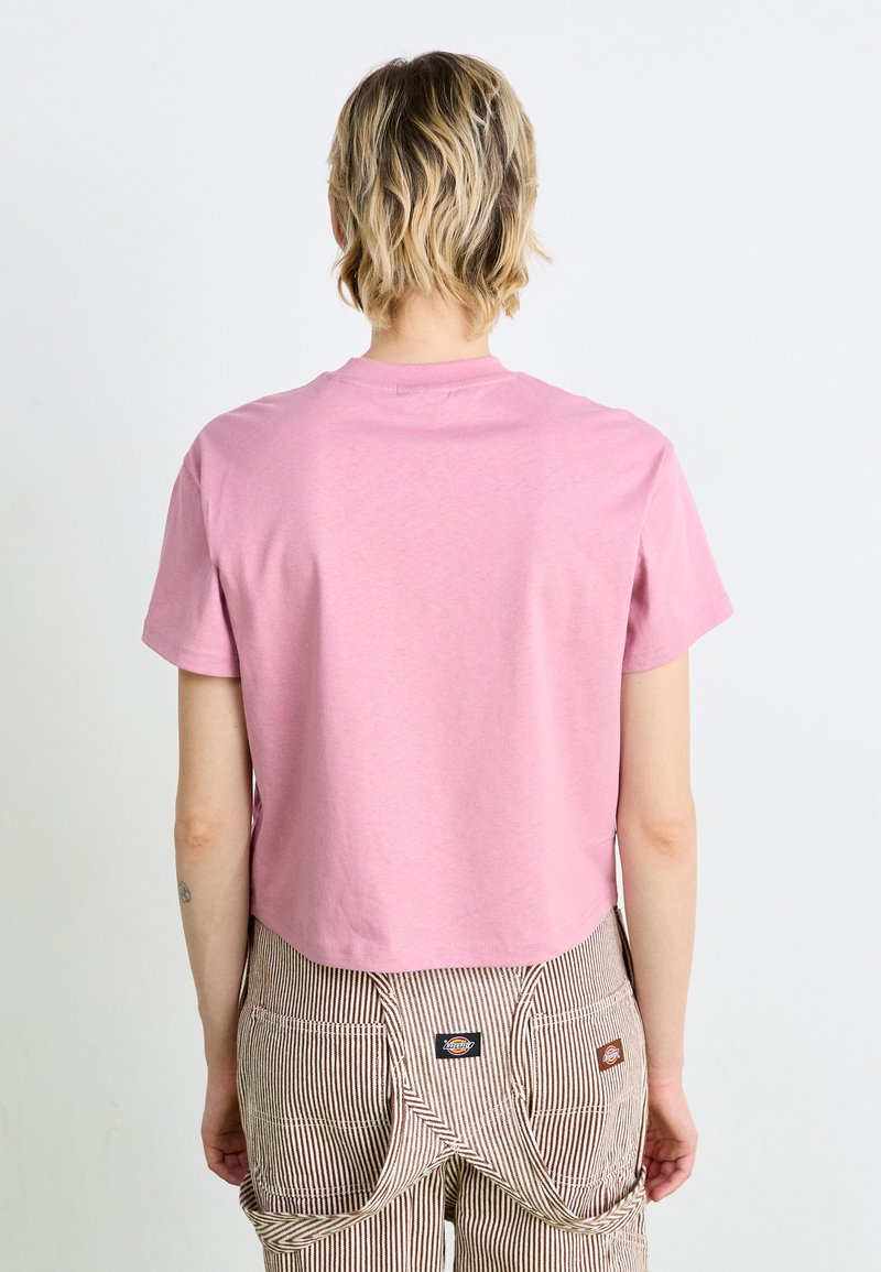 T-shirt crop in cotone rosa con maniche corte, texture liscia e scollatura rotonda, abbinato a salopette a strisce con grandi tasche.