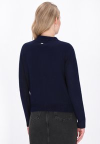 Navy blue sweater, soft knit fabric, relaxed fit, ribbed cuffs and hem, small metal accent on back, paired with dark gray skirt.