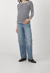 Randig långärmad topp i marinblått och vitt med knapppdetaljer, tillsammans med ljusblå vida jeans och svarta klackiga ankelskor.