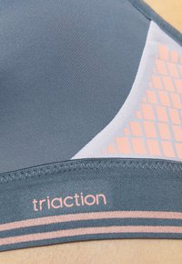 Hallhalli halli spordirinnahoidja, millel on sile tekstuur, roosa geomeetriliste aktsentidega ja riba, millel on kiri 'triaction'. Sisaldab kontrastset valget paneeli.