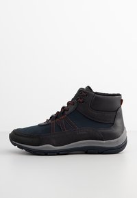 Zapatillas altas en material sintético azul marino y negro con costuras marrones. Presentan un acabado texturizado y una suela de goma para mayor agarre.
