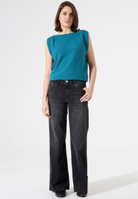 Top sin mangas de color verde azulado con escote cuadrado, combinado con jeans de mezclilla negros de corte holgado y zapatos negros.