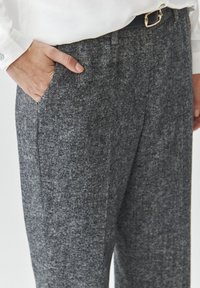 Gray textured trousers with a subtle pattern, featuring side pockets and a belt loop, paired with a white long-sleeve top.