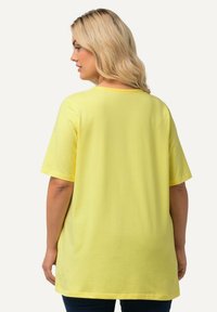 T-shirt giallo in cotone con maniche corte e scollatura tonda. Vestibilità ampia con una texture liscia, che arriva fino all'altezza dei fianchi.