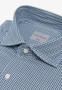 Camisa ajustada hecha de tela texturizada en un patrón de cuadros azul y blanco; cuenta con un collar puntiagudo, dos botones frontales y una etiqueta.