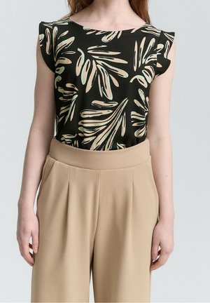 Kobieta ubrana w czarny top bez rękawów z beżowymi i jasnozielonymi wzorami liści, w połączeniu z beżowymi szerokimi spodniami z wysokim stanem.