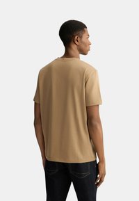 T-shirt beige a maniche corte realizzato in morbido cotone, con scollatura rotonda e vestibilità rilassata, abbinato a jeans scuri.